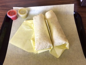 two tacos wrapped up and salsa in cups.